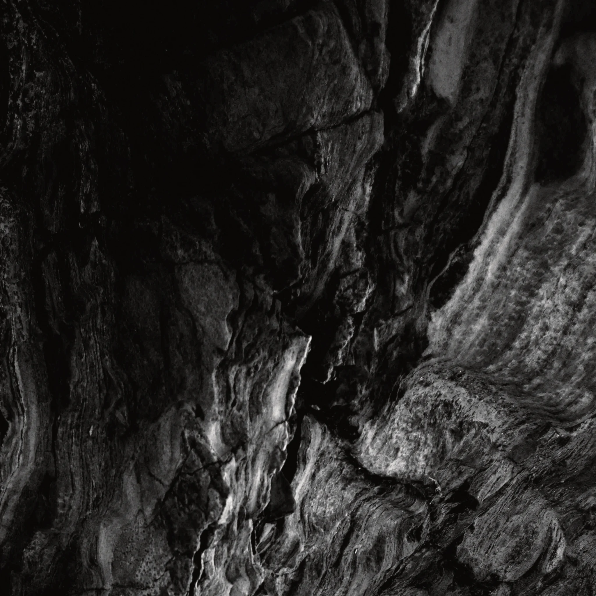 A black and white abstract close-up of a marble rock face, highlighting natural cracks, shadows and texture.