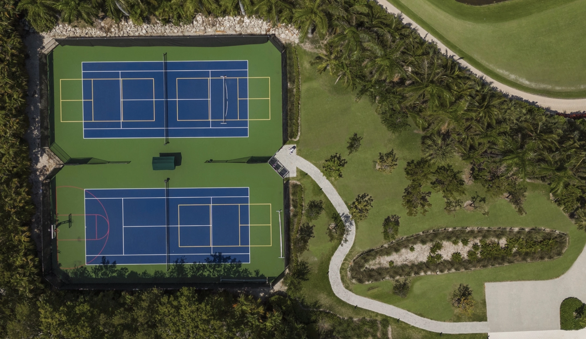 Aerial view of the tennis courts at the Mondrian HB Residences with pickle ball lines and shaded seating.